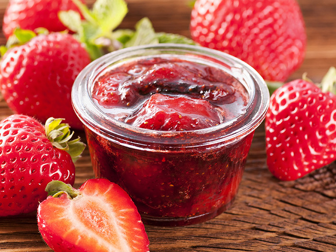 Image d'un pot de confiture aux fraises accompagné de fraises sur un plateau en osier déposé sur une table